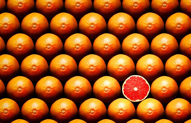 many rows of whole grapefruits with one sliced grapefruit